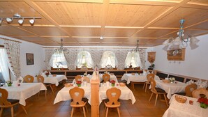 A dining area with multiple tables and chairs, wooden ceiling, and decorative curtains.
