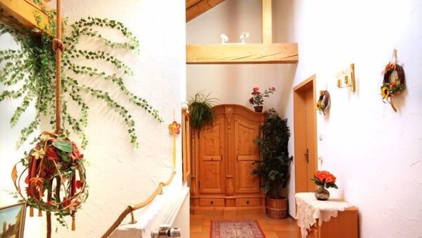 A wooden staircase with a red patterned rug leading to a room with a wooden door and a plant.