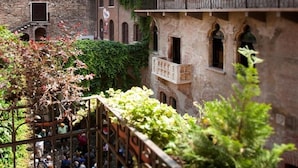 A courtyard with a brick building featuring arched windows and balconies, surrounded by greenery. - Relais Balcone di Giulietta (Verona)