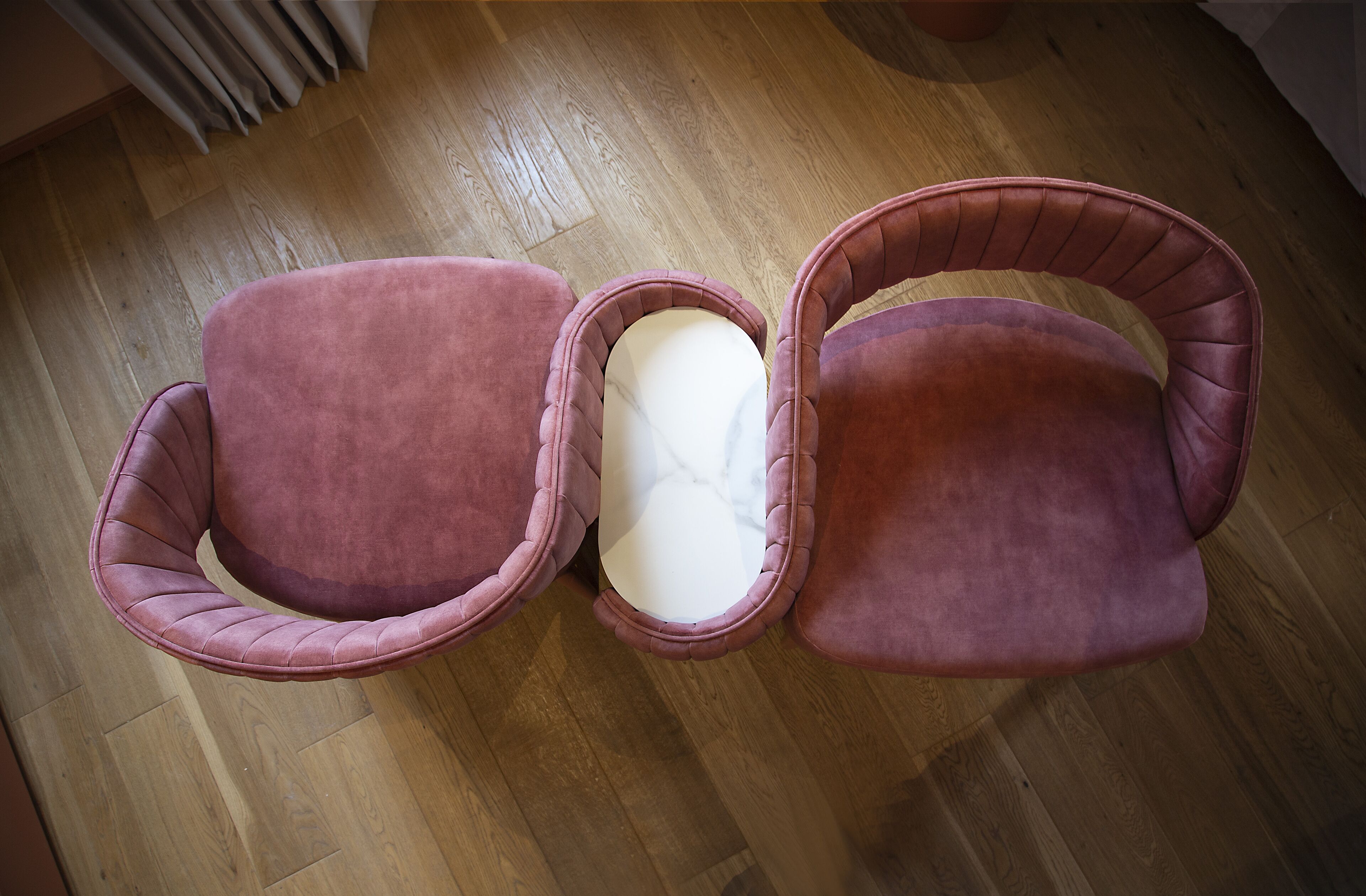 Una habitación con suelo de madera y un sillón rosa con cojín blanco.