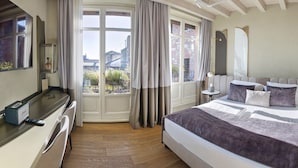 A hotel room with a bed, bedside tables, a desk with a computer, a TV, and a view of the city through large windows. - Relais Balcone di Giulietta (Verona)