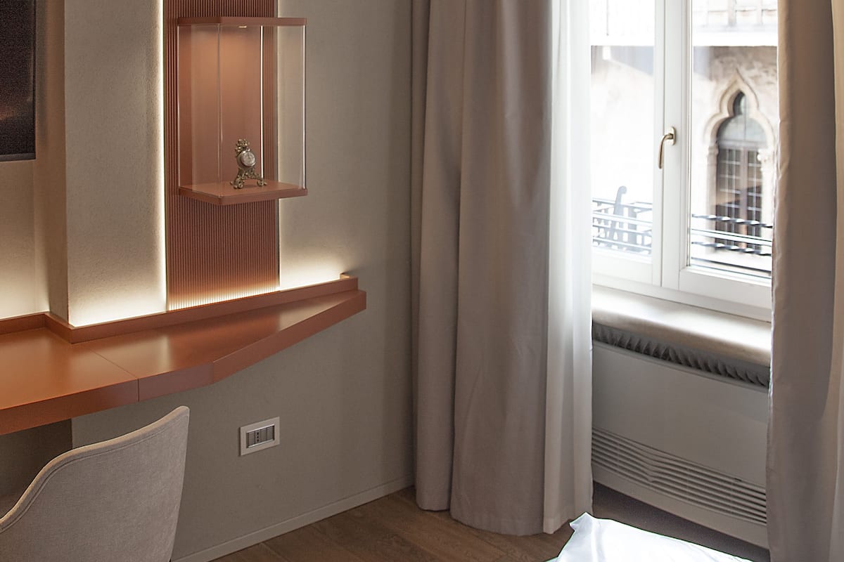 A hotel room with a built-in shelf, a window with curtains, and a view of the cityscape.