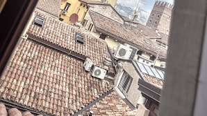 A view through a window of a building with a tower, terracotta rooftops, and a clear sky. - Relais Balcone di Giulietta (Verona)