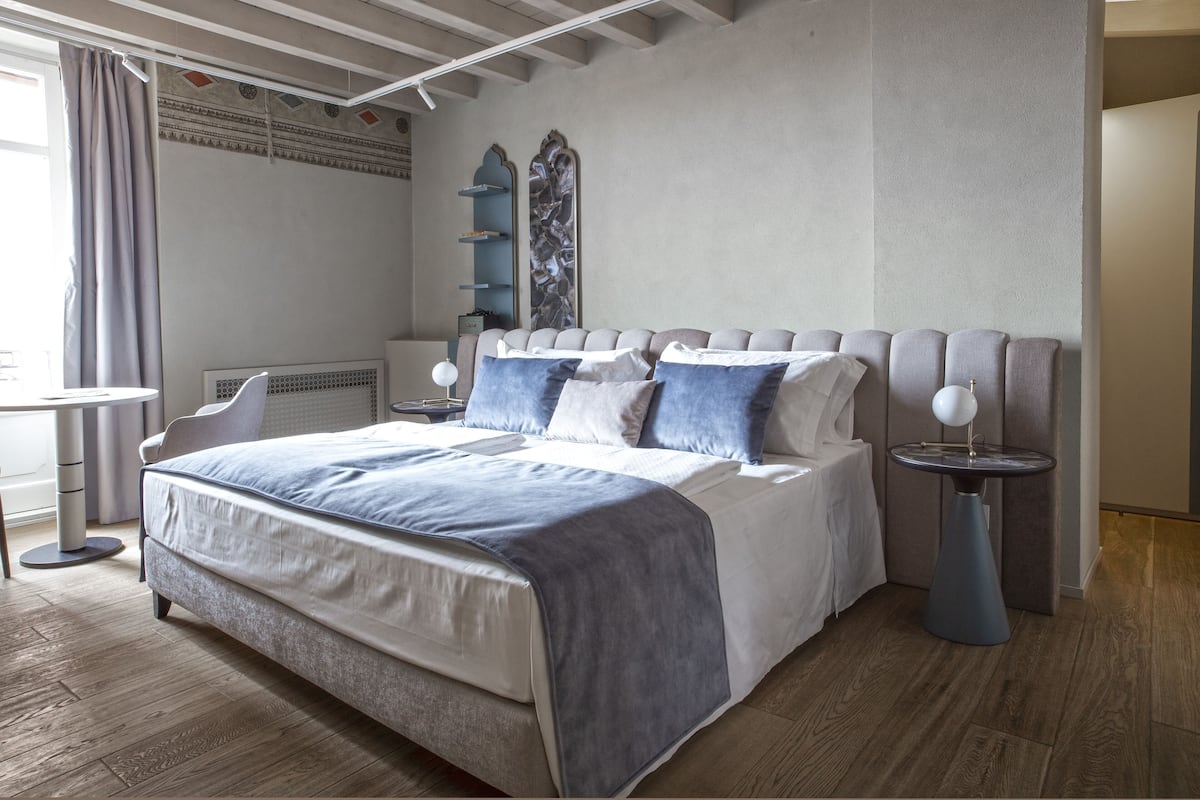 A modern bedroom with a large bed, bedside tables, a chair, and a decorative wall piece.