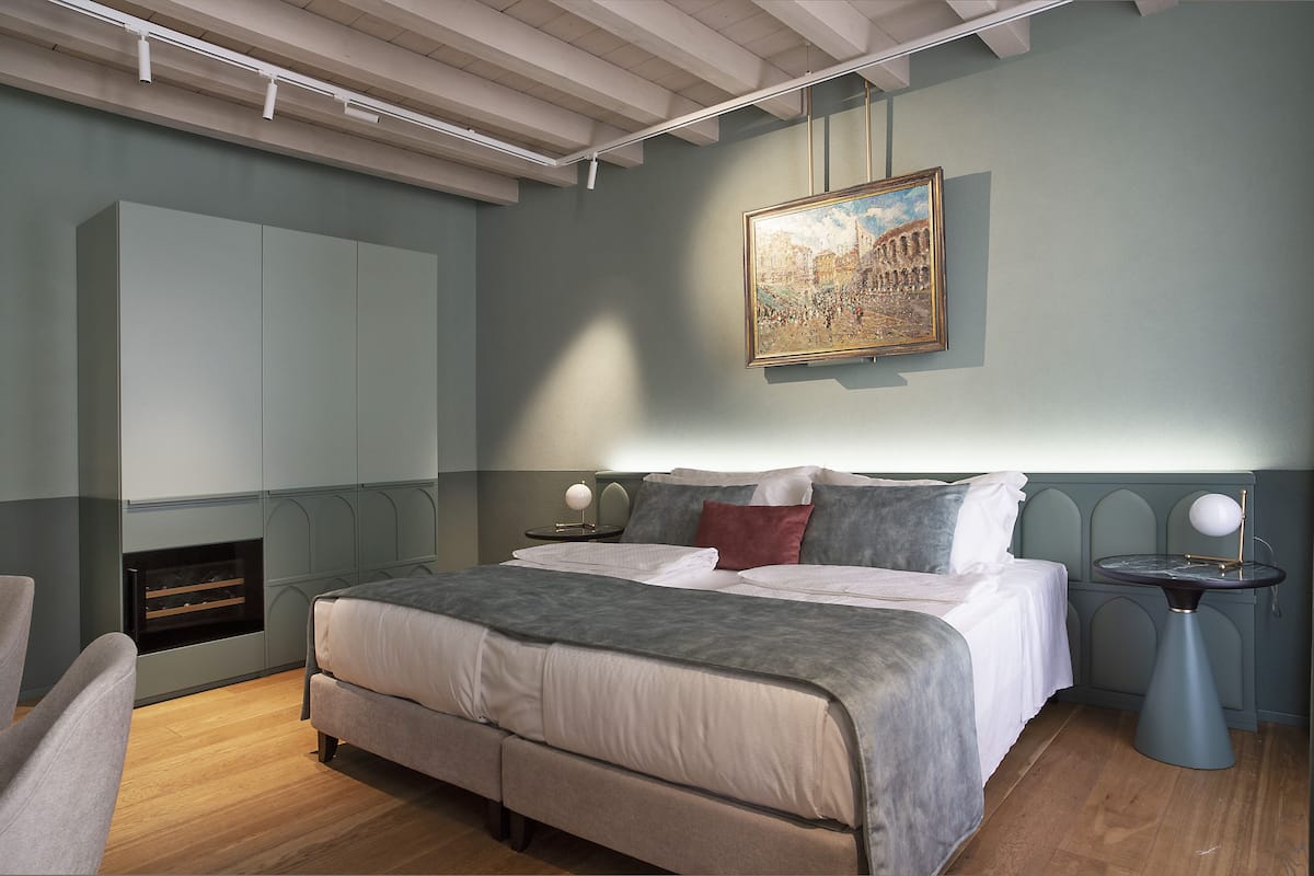 A bedroom with a large bed, a nightstand with a lamp, a painting on the wall, and built-in cabinets.
