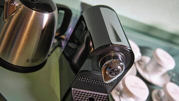 A close-up of a coffee machine and a kettle on a countertop with tea bottles in the background.