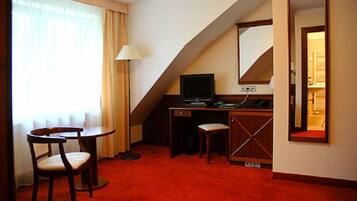A hotel room with a desk, chair, and a large mirror.