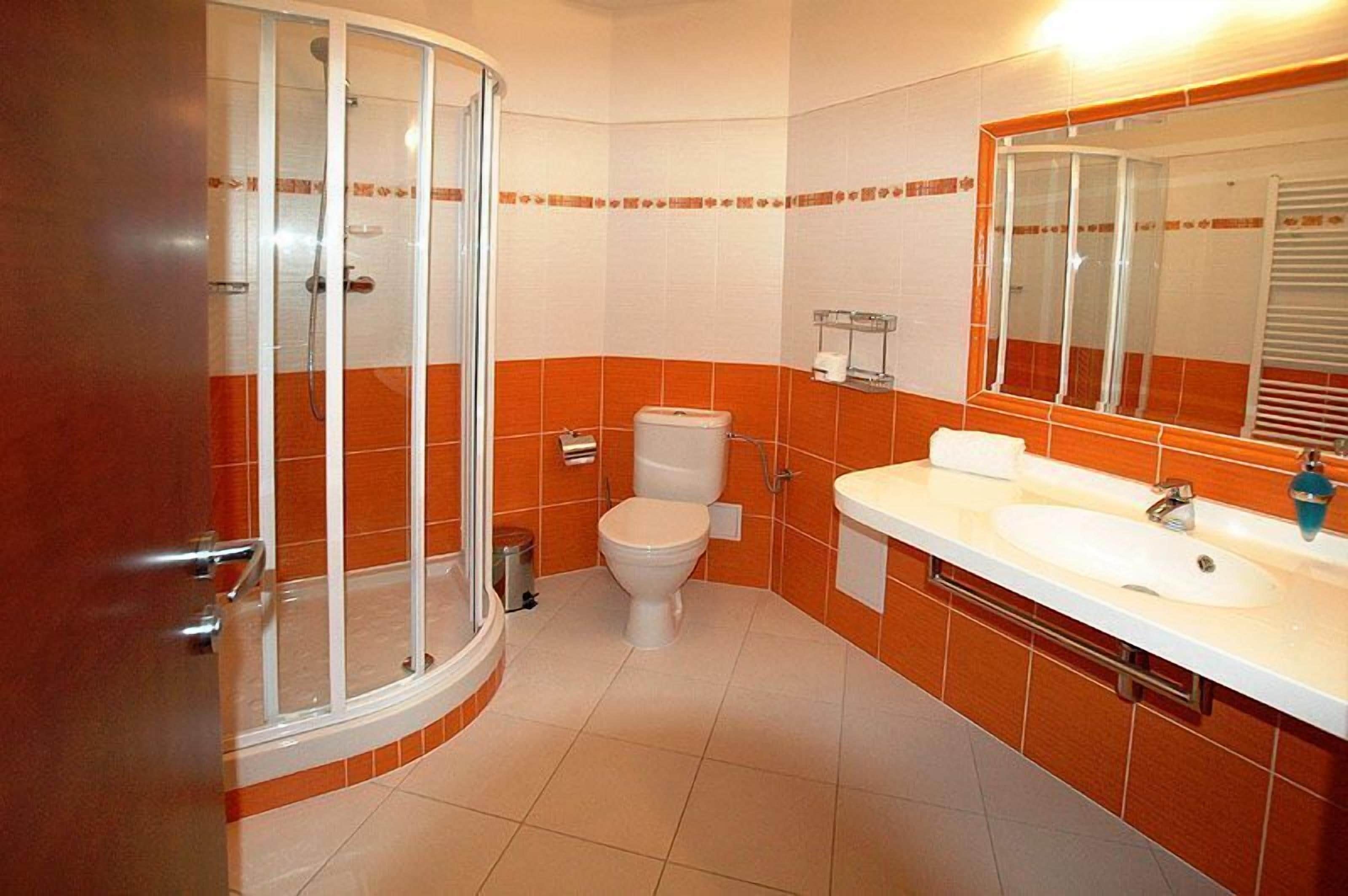 Un baño con cabina de ducha de vidrio, inodoro y lavamanos con espejo.