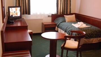 A hotel room with a bed, a desk with a chair, a small table, and a television.