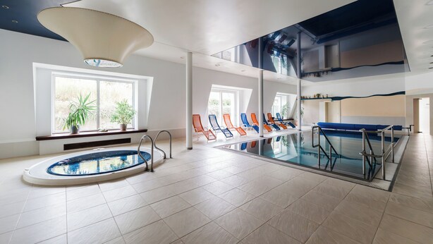 An indoor swimming pool with a glass barrier, lounge chairs, and a ceiling light fixture. - Hotel Komorni Hurka (Cheb)