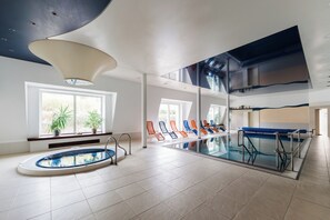 An indoor swimming pool with a glass barrier, lounge chairs, and a ceiling light fixture. - Hotel Komorni Hurka (Cheb)