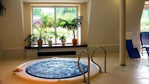 A spa area with a hot tub, a window with plants, and a view of greenery. - Hotel Komorni Hurka (Cheb)