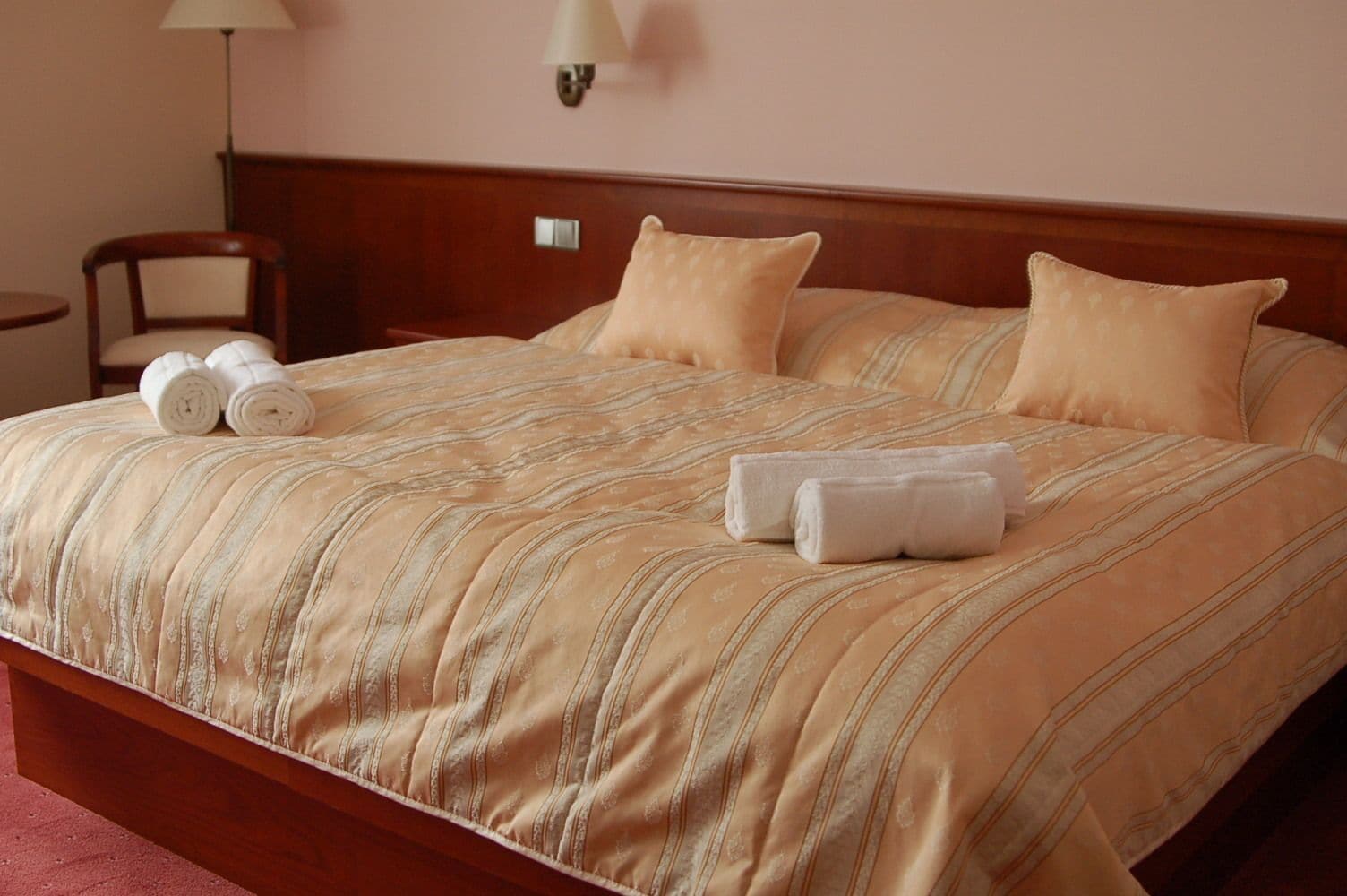 Un letto ben rifatto con lenzuola a righe e due cuscini, una testiera in legno e un comodino con una lampada e asciugamani arrotolati.