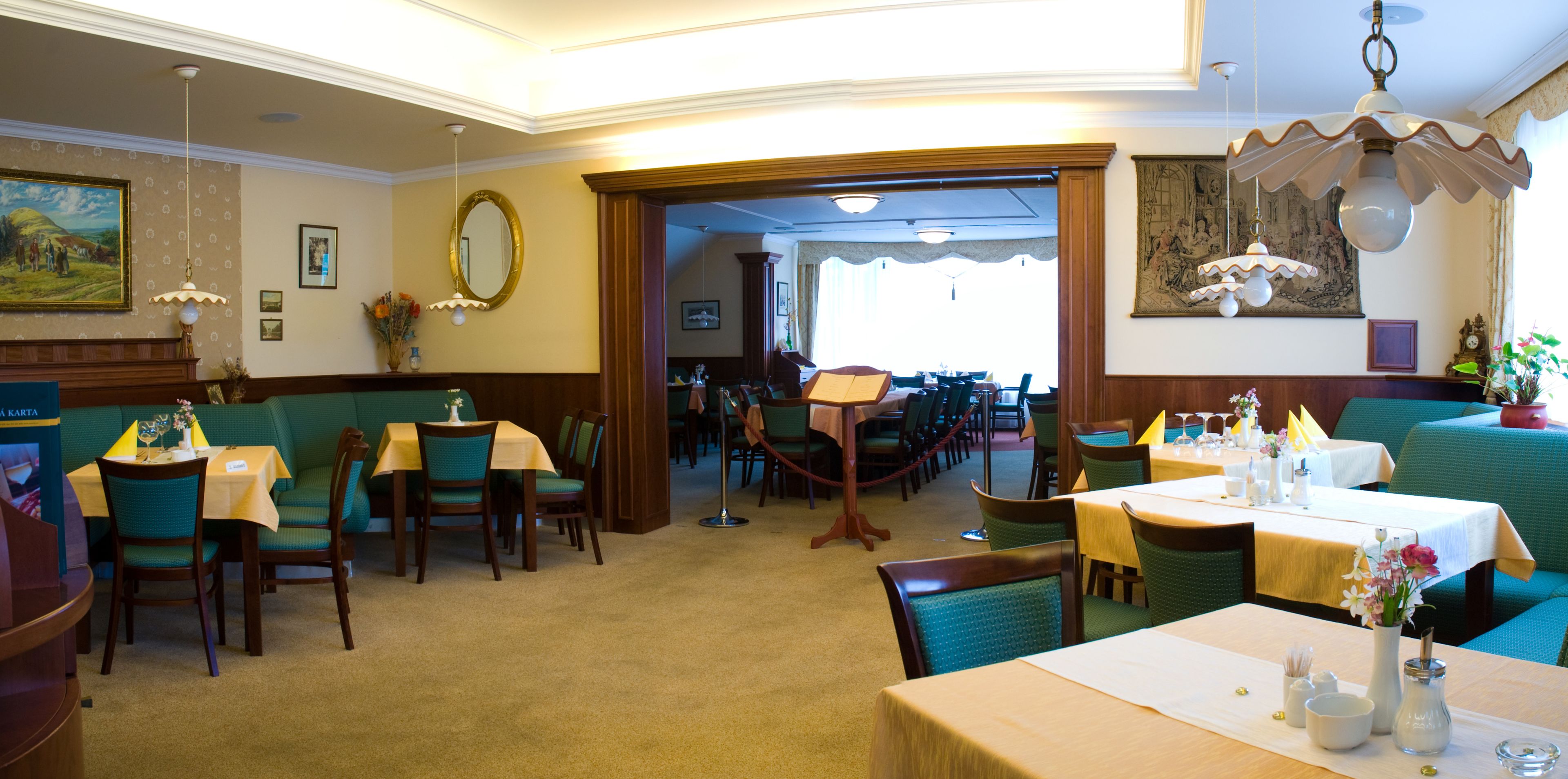 Ein Restaurant mit Sitzecken und Tischen, einer Kristallleuchter und einem Gemälde an der Wand.