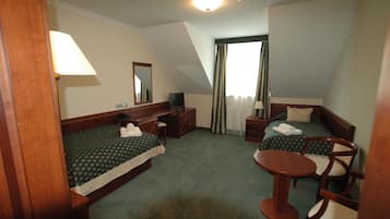 A hotel room with two single beds, a desk, a chair, a small table, a television, and a window with curtains.