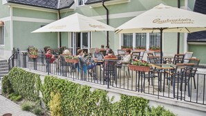 An outdoor seating area with tables and chairs under umbrellas, surrounded by a low fence. - Hotel Komorni Hurka (Cheb)