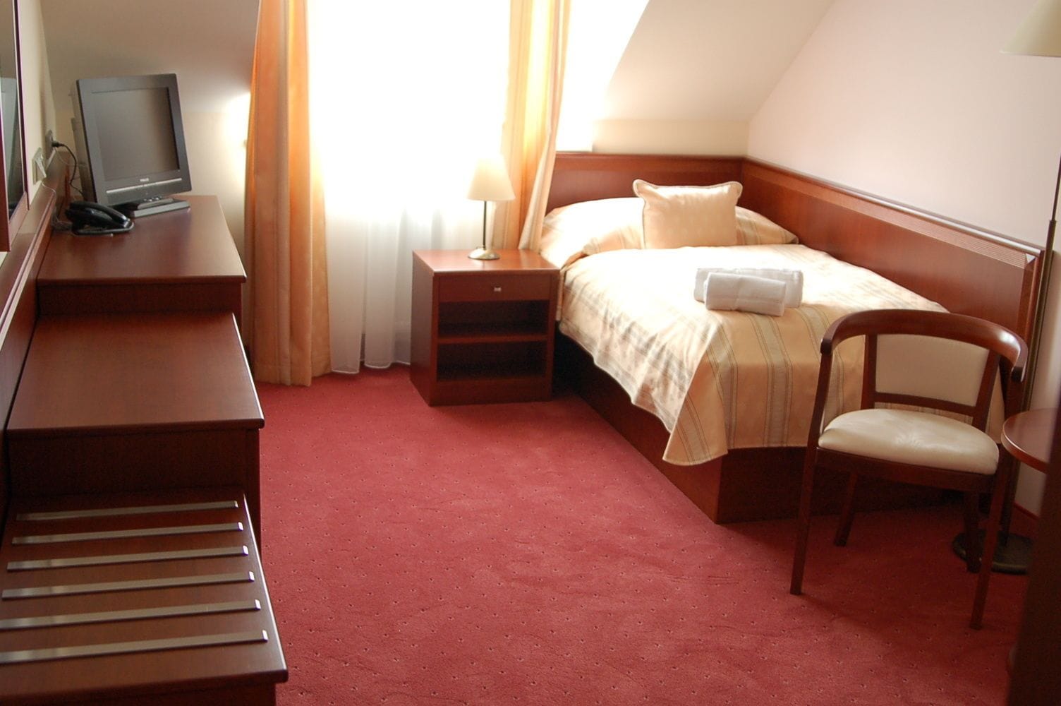 Una habitación de hotel con una cama, un escritorio con ordenador, una silla y una mesita de noche.