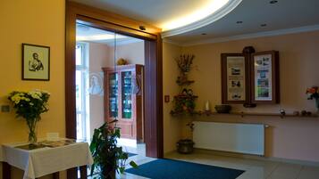 A reception area with a table, a vase with flowers, a potted plant, a wooden cabinet, and a wall with framed pictures and information displays.