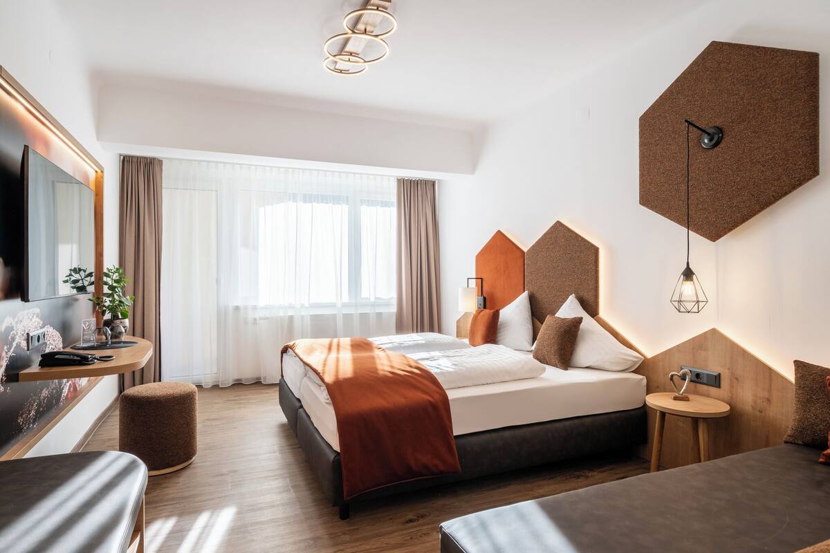 Quarto de hotel moderno com uma cama grande, uma escrivaninha, um banquinho redondo e uma televisão.