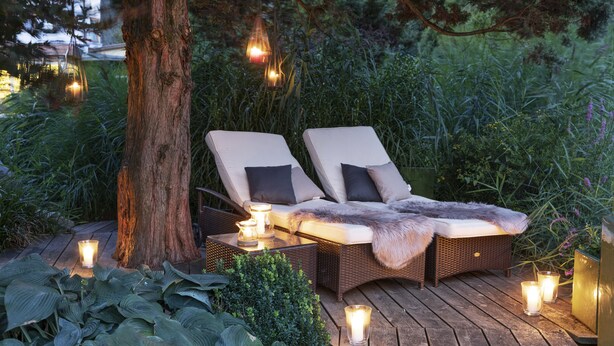 A wooden deck with two lounge chairs, a tree, and candles. - Ferienhotel Trattnig GmbH (Radenthein)