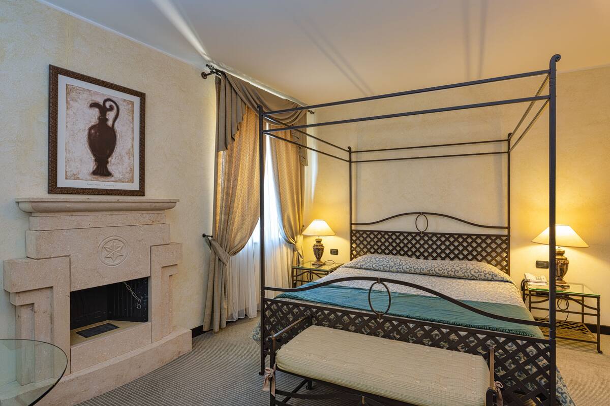 A four-poster bed with a headboard, a fireplace, and two bedside tables with lamps.