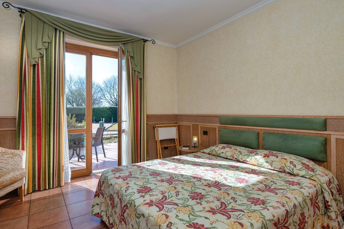 A hotel room with a bed, a small desk, and a view of the outdoors.