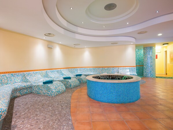 A spa area with a mosaic-tiled bench, a circular hot tub, and a tiled floor.