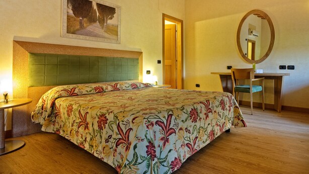 A hotel room with a bed, a desk, a chair, a mirror, and a painting on the wall. - Active Hotel Paradiso (Castelnuovo del Garda)