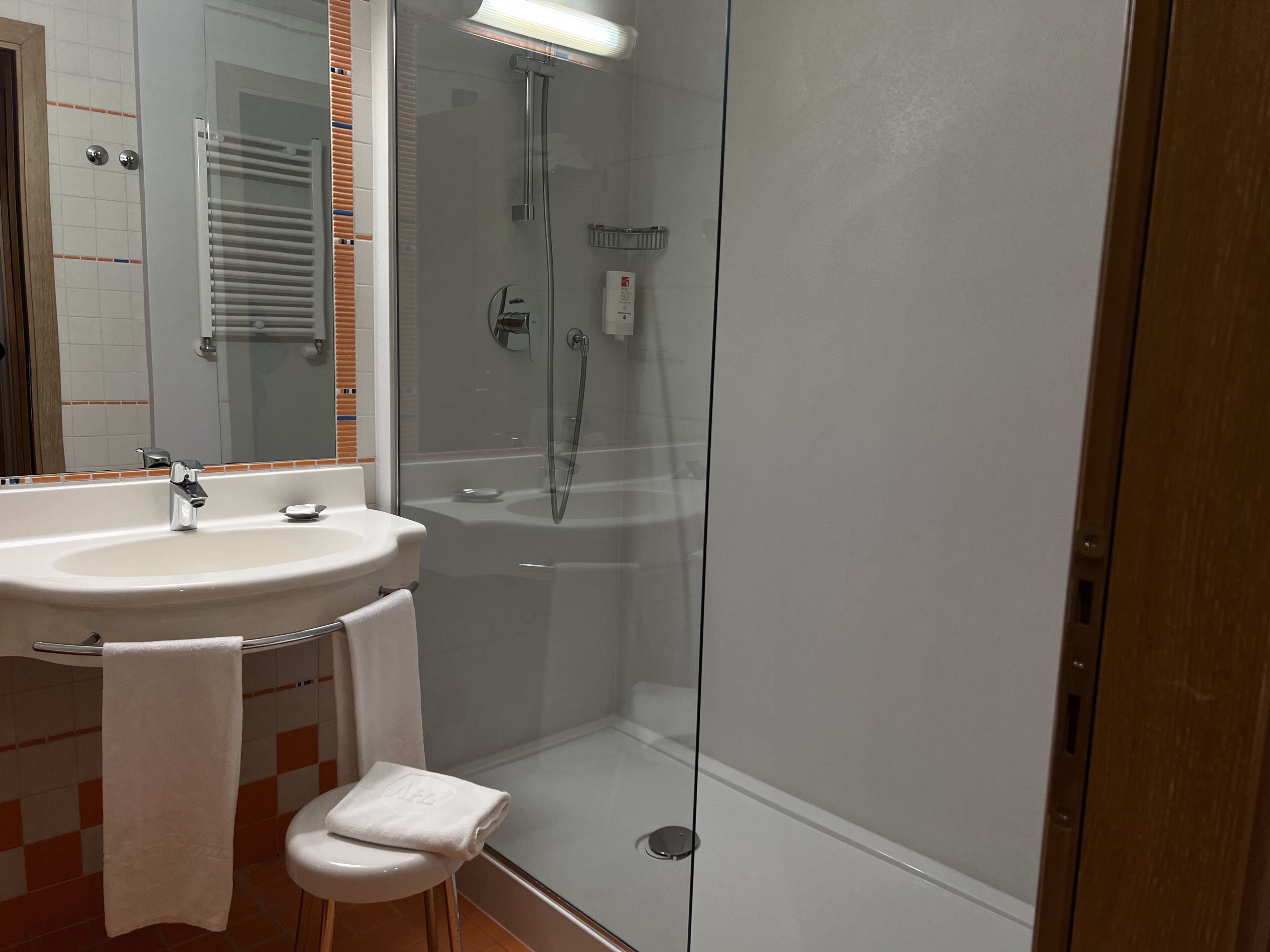 Een badkamer met een douche met glazen wand, een wastafel en een spiegel.