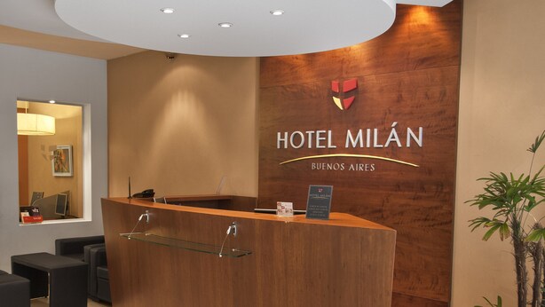 A hotel reception desk with a wooden finish, a modern ceiling design, and a sign reading "HOTEL MILÁN BUENOS AIRES". - Milan Hotel (Buenos Aires)