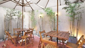 A wooden table and chairs under a large umbrella in a covered outdoor area with bamboo plants. - Milan Hotel (Buenos Aires)