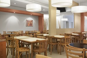 A restaurant interior with multiple wooden tables and chairs, pendant lighting, and a large mirror on the wall. - Milan Hotel (Buenos Aires)