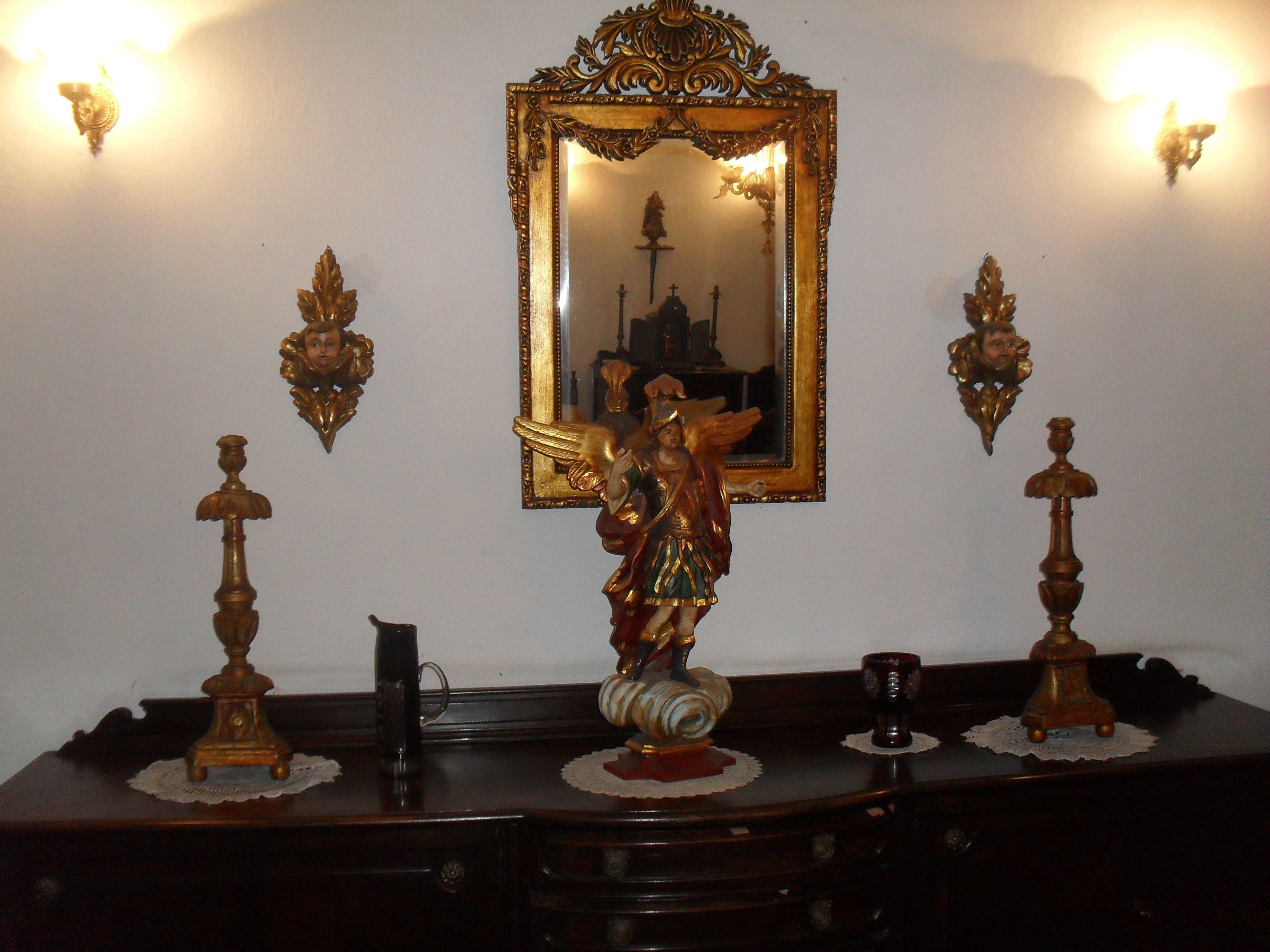 Un aparador de madera con espejo, candelabros ornamentales y una pequeña estatua.