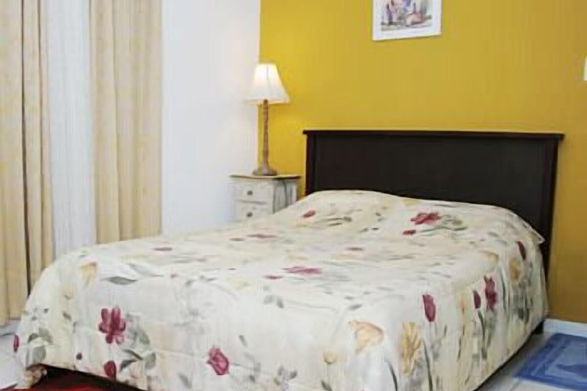 A bedroom with a floral bedspread, a bedside table with a lamp, and a picture on the wall.