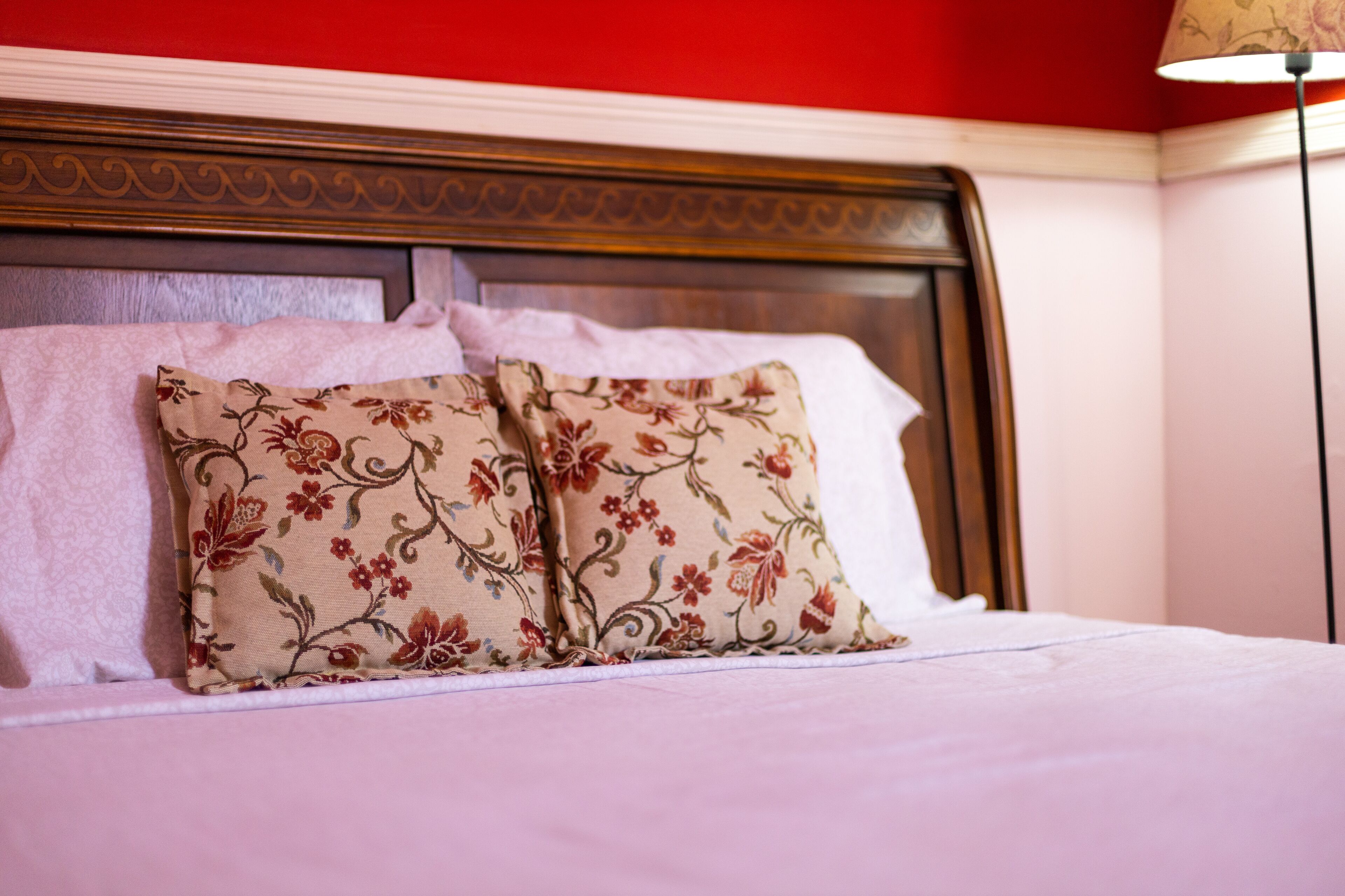 Una cama bien hecha con almohadas estampadas con motivos florales y un cabecero de madera.