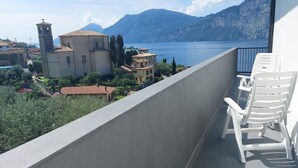 Varanda com cadeiras brancas com vista para um lago, edifícios e montanhas.