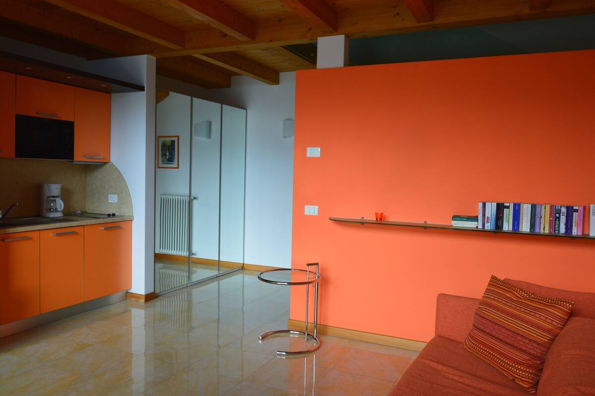 A modern kitchen with orange cabinets, a coffee maker, and a round metal table.