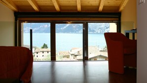 Quarto espaçoso com teto de madeira e grandes portas de vidro deslizantes que dão para uma varanda com vista para o mar e as montanhas.