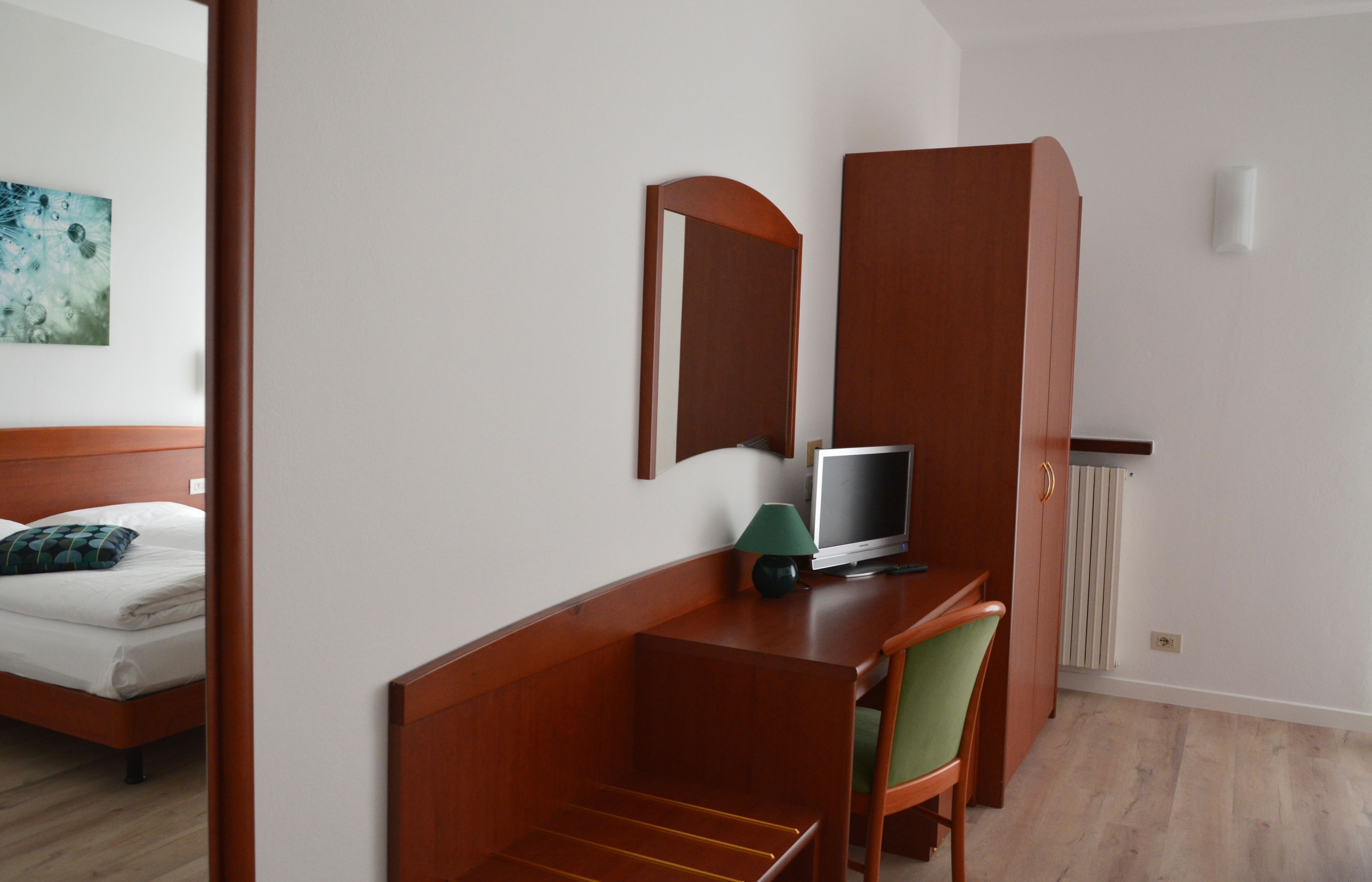 Une chambre d’hôtel avec un lit, un bureau avec un ordinateur, une chaise, un miroir et un radiateur.