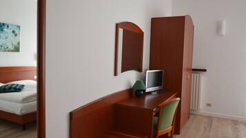 Une chambre d’hôtel avec un lit, un bureau avec un ordinateur, une chaise, un miroir et un radiateur.