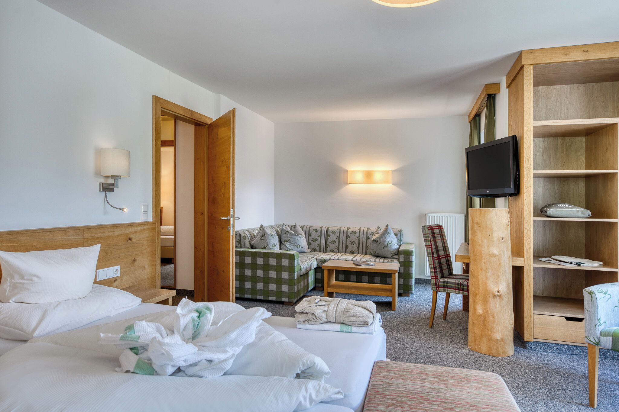 A hotel room with a bed, a sofa, a television, and a wooden bookshelf.