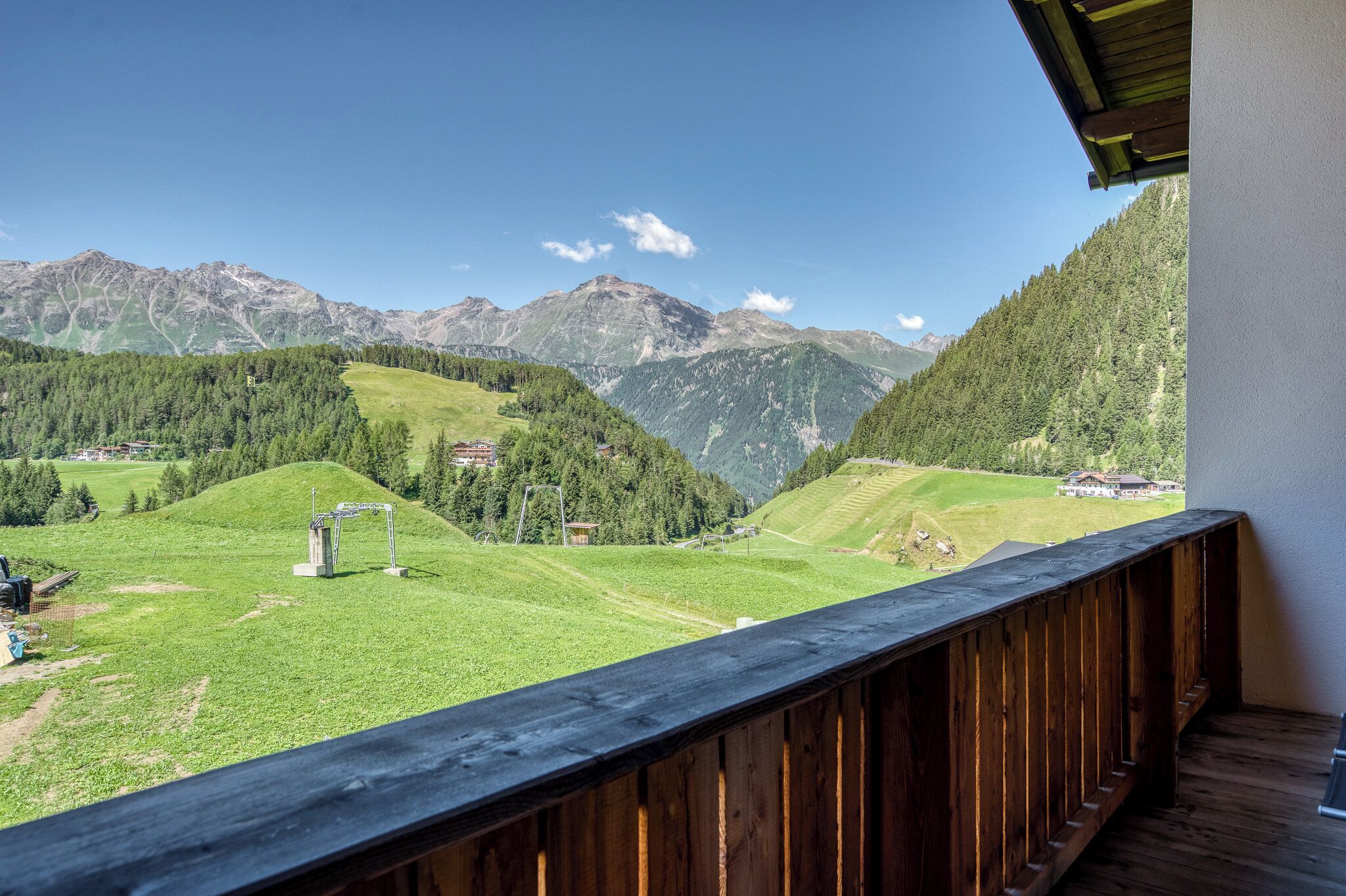 Un balcon offrant une vue sur un paysage montagneux, avec des champs verdoyants et quelques bâtiments.