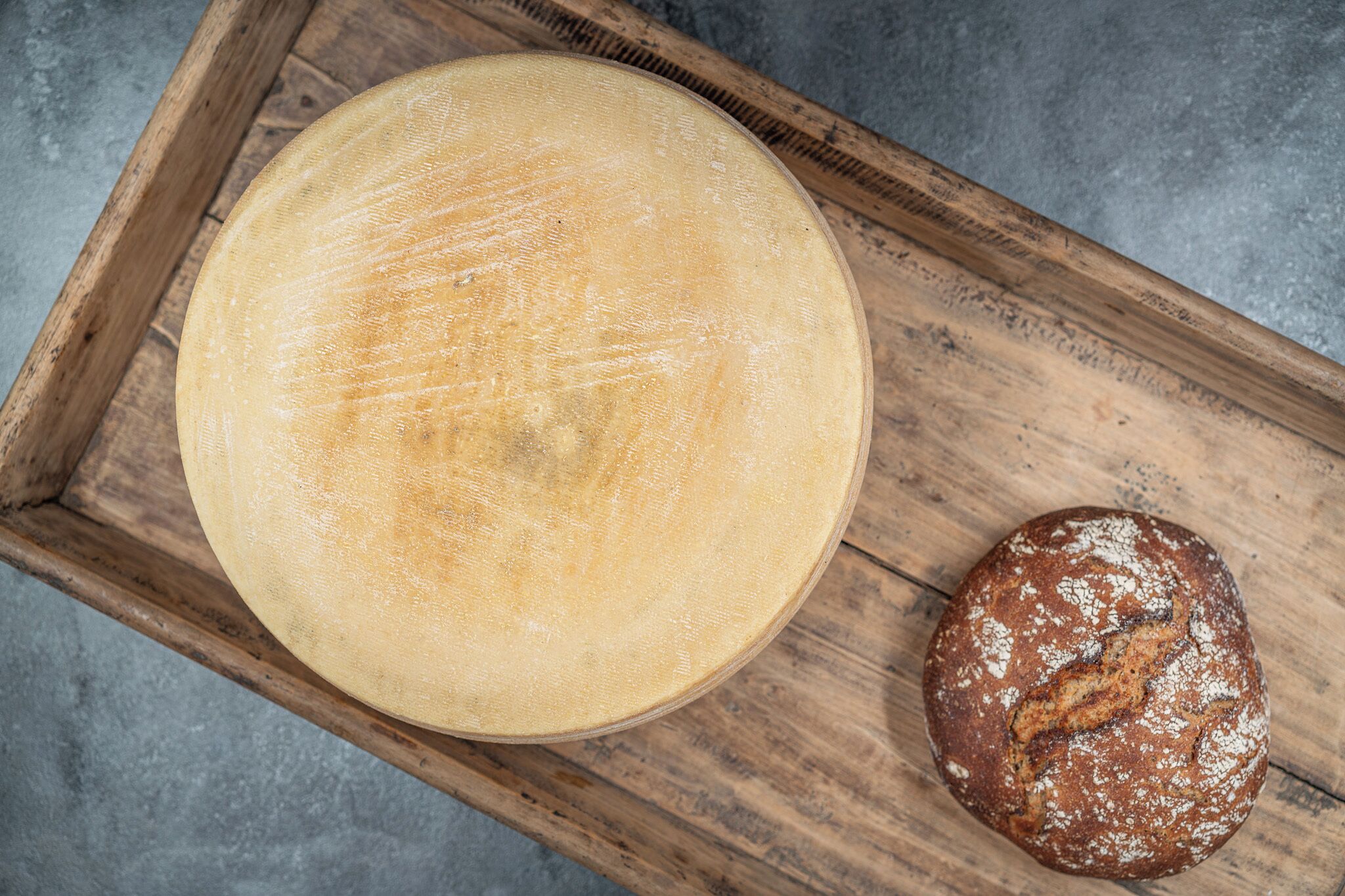 A round cheese on a wooden board with a loaf of bread beside it.