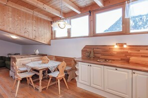 Ein Holzinnenraum mit Esstisch, Stühlen, einer Küchenzeile und großen Fenstern.