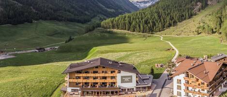 Un hôtel à plusieurs étages doté d’un télésiège, entouré de collines verdoyantes et de montagnes.