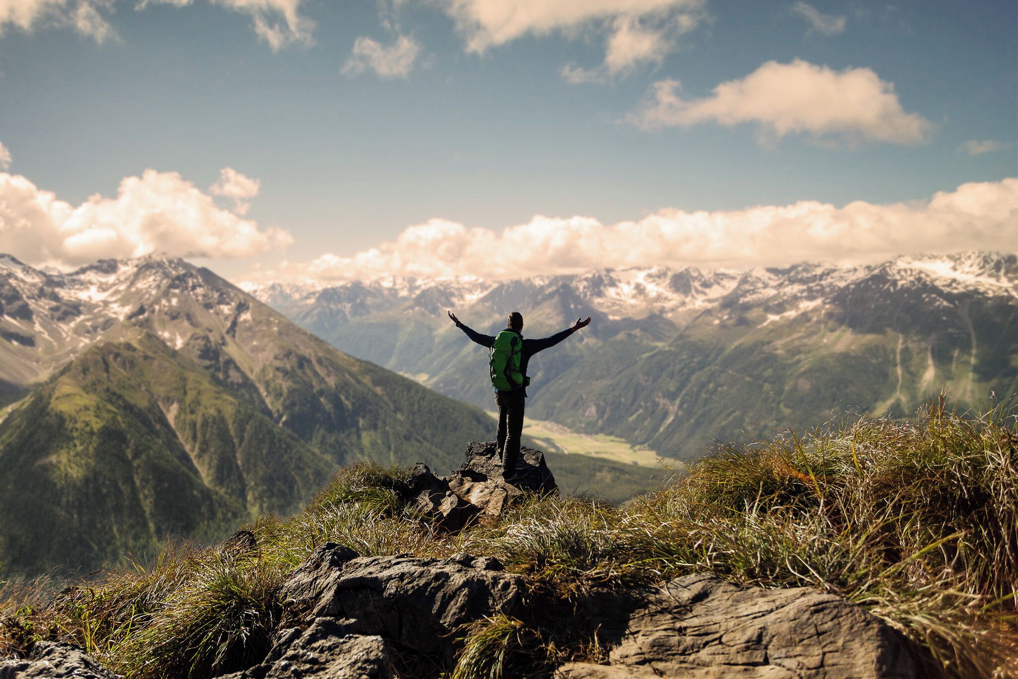 A person standing on a rocky outcrop with arms outstretched, overlooking a mountainous landscape.