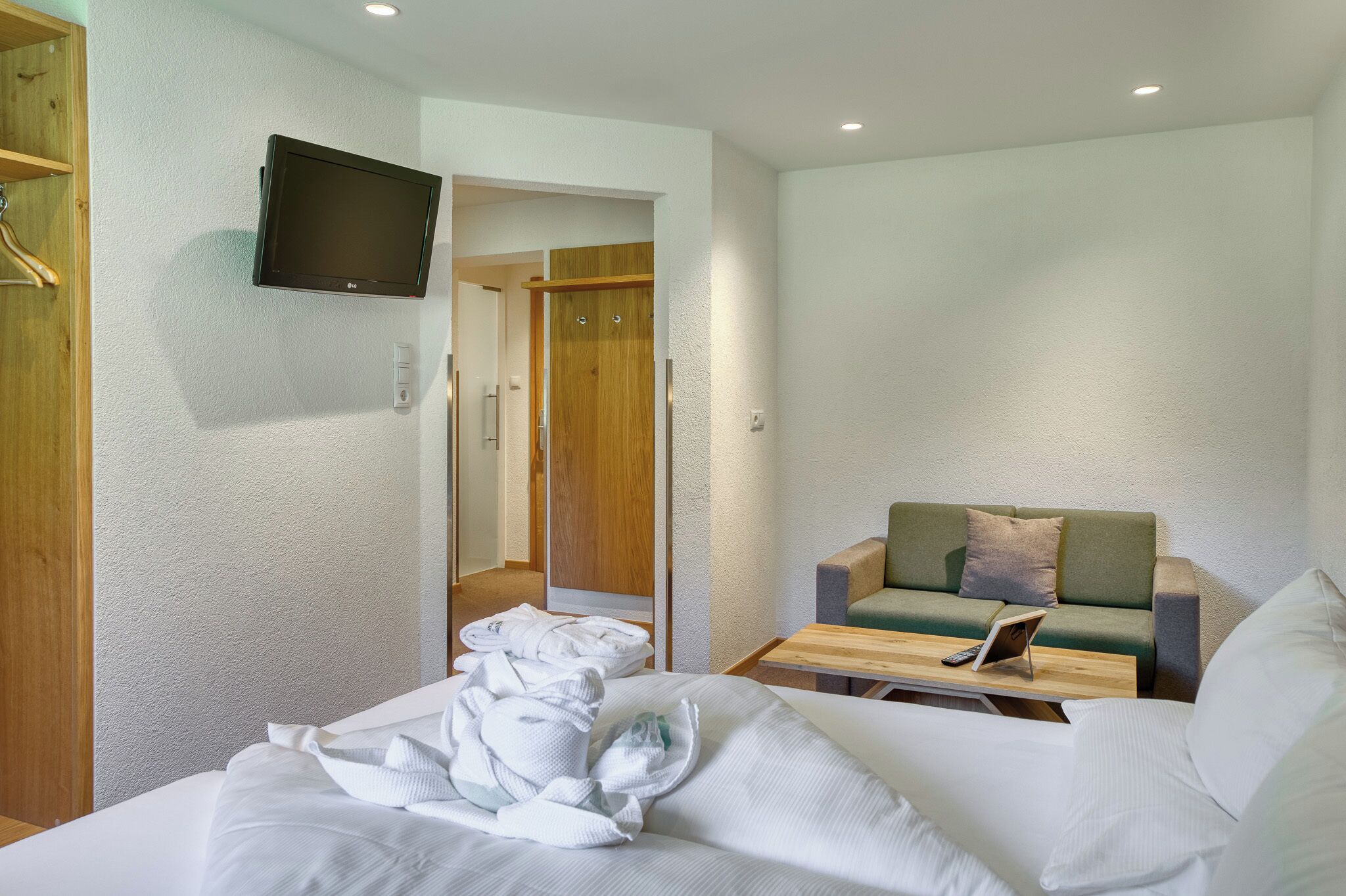 Une chambre d’hôtel avec un lit, un canapé, un téléviseur fixé au mur et une porte en bois.