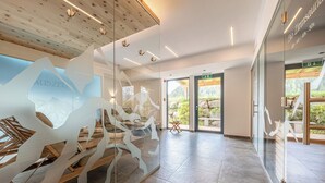 A modern interior with a glass wall displaying a mountain design, a wooden ceiling, and a view of an outdoor area. - Hotel Falknerhof (Umhausen)