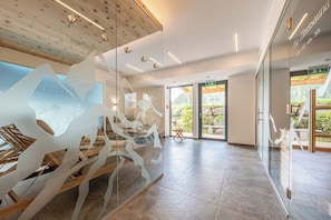 A modern interior with a glass wall displaying a mountain design, a wooden ceiling, and a view of an outdoor area. - Hotel Falknerhof (Umhausen)
