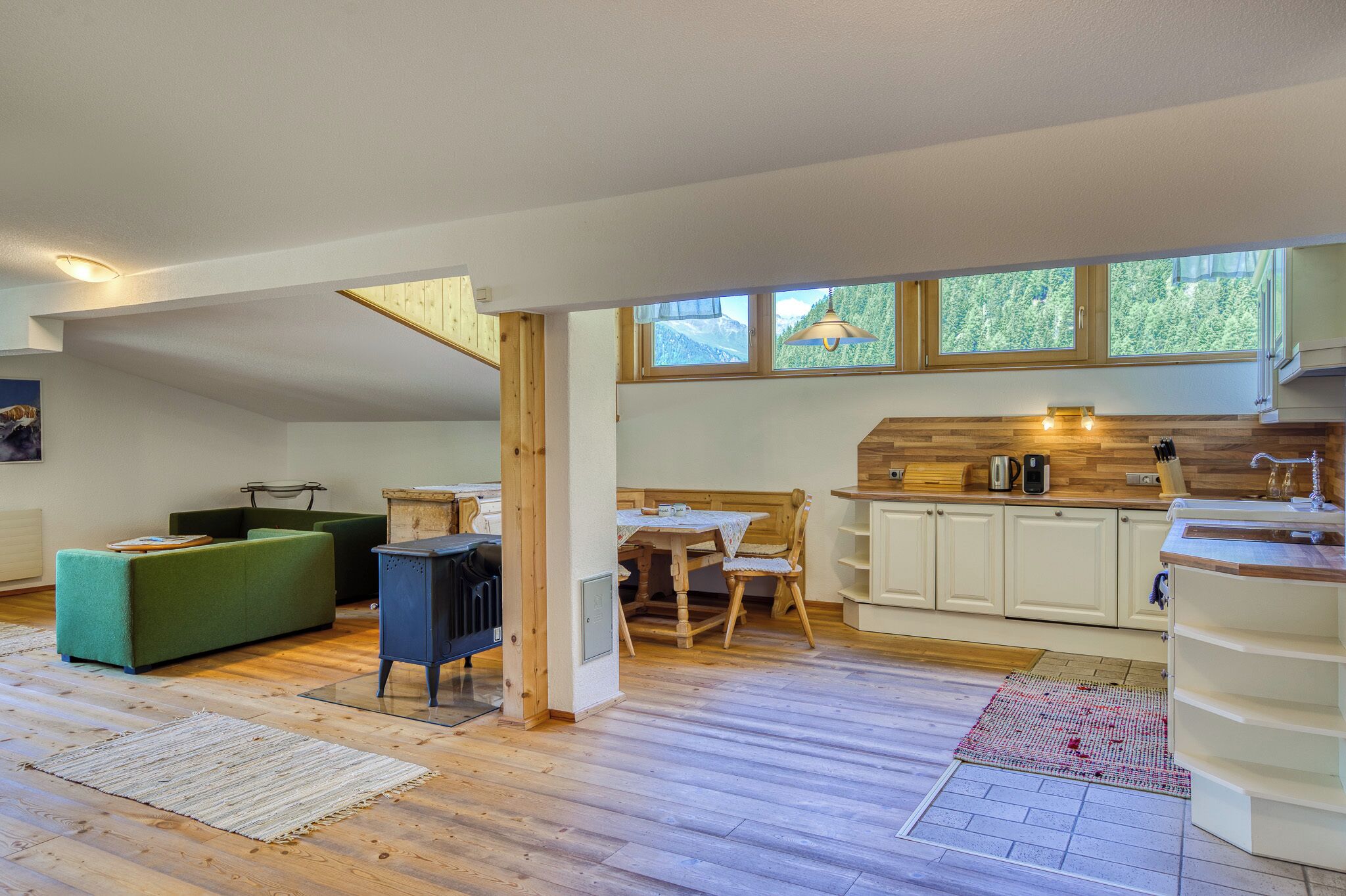 Un interno moderno con cucina, zona pranzo e soggiorno, caratterizzato da pavimento in legno, mobili bianchi e ampie finestre.